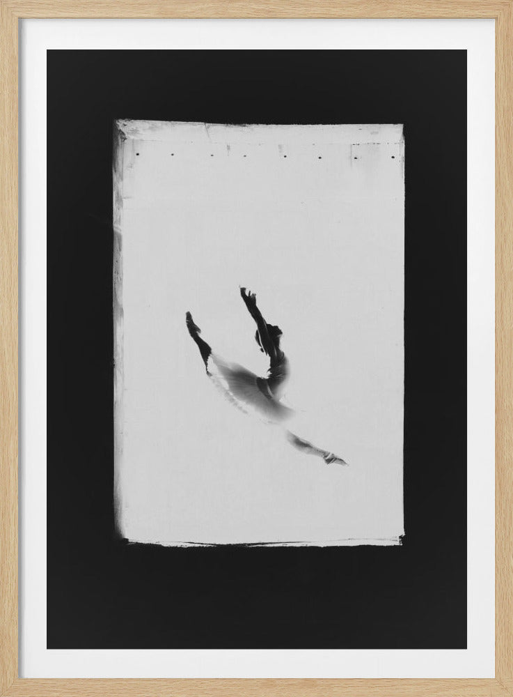 A framed black and white photograph of a ballerina in a graceful, floating pose against a bright, soft-focus background. The artwork has a textured, canvas-like appearance with rough edges and is set within a wide black mat and a simple black frame. Artwork