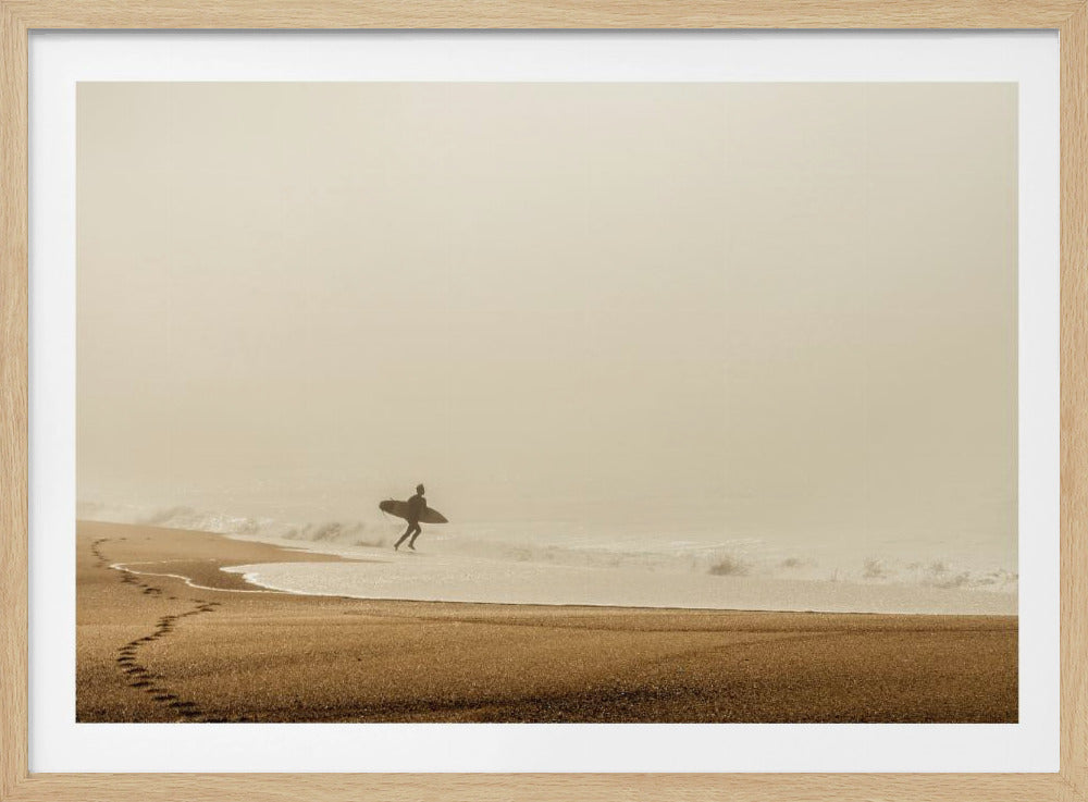 A minimalist photograph of a silhouetted surfer carrying a surfboard, running into the ocean on a foggy morning. The scene has a warm, sepia tone, with footprints visible in the wet sand in the foreground and a vast, misty sky. Wall Art