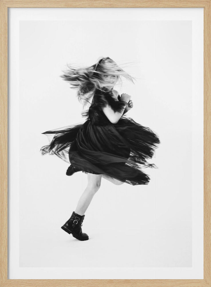 A dynamic black and white photograph of a girl in a black dress and combat boots, caught mid-motion with her hair and skirt flying around her against a stark white background. Artwork