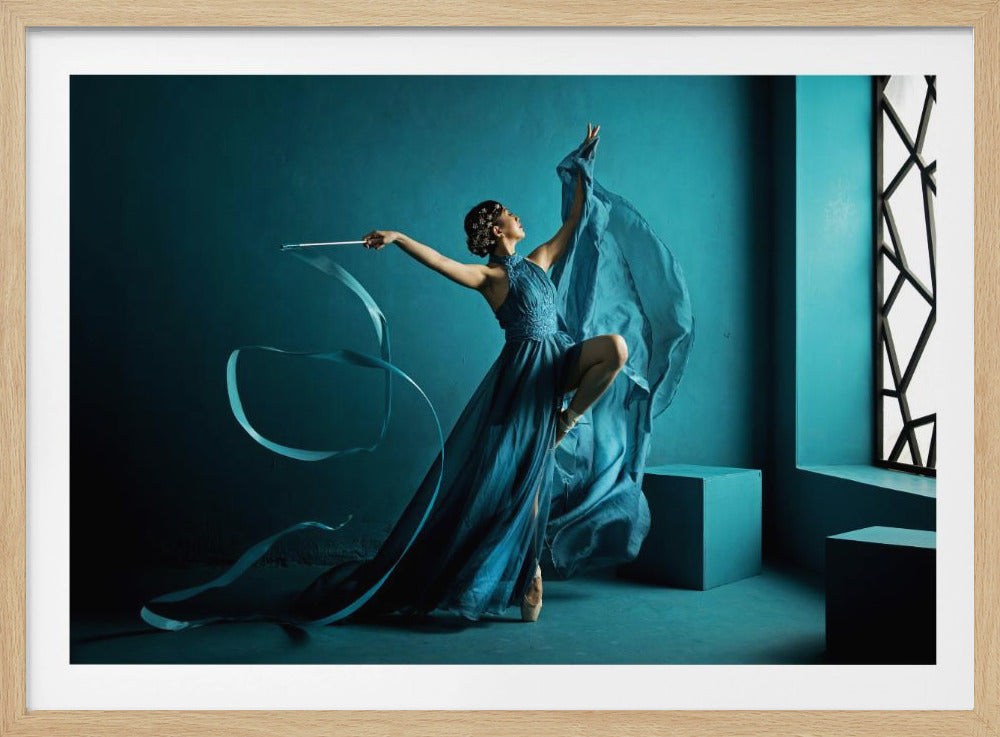 A framed photograph of a graceful ballerina in a flowing teal-blue gown, posing elegantly on one pointe shoe. She holds a ribbon wand, with the ribbon swirling around her, against a monochromatic blue background with geometric blocks and a stylized window. Decor
