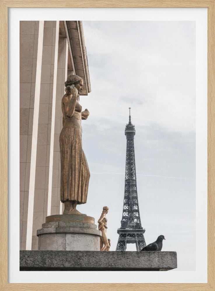 A vertical photograph of a bronze statue of a woman standing on a stone pedestal, with the Eiffel Tower visible in the background against a pale, overcast sky. A single pigeon is perched on a ledge in the foreground. Wall Art