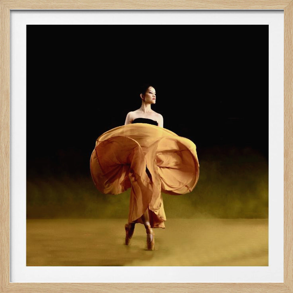 A framed photograph of a ballerina mid-pose against a dark background. She is on pointe, wearing a black top and a voluminous golden-yellow skirt that is dramatically billowing out around her, caught in a moment of motion. The floor has a hazy golden glow, and the entire scene has a theatrical, focused lighting. Artwork