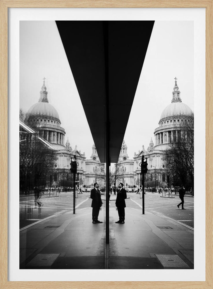 A surreal black and white photograph capturing a symmetrical reflection of a city scene, with St. Paul's Cathedral prominently featured on both sides. A dark, V-shaped reflection from a building divides the image vertically. In the foreground, the reflection of two men in dark suits standing on the sidewalk adds a human element to the grand architectural view. Decor