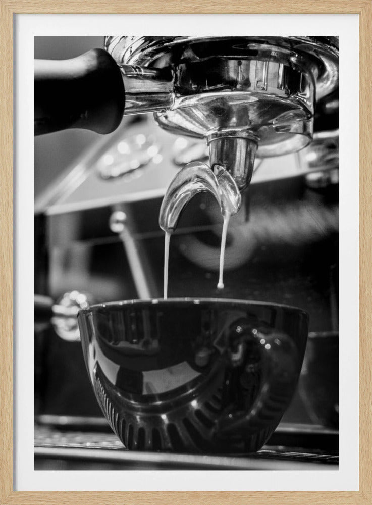 A close-up, black and white photograph of an espresso machine pouring two streams of fresh coffee from a chrome portafilter into a dark, glossy cup. Print