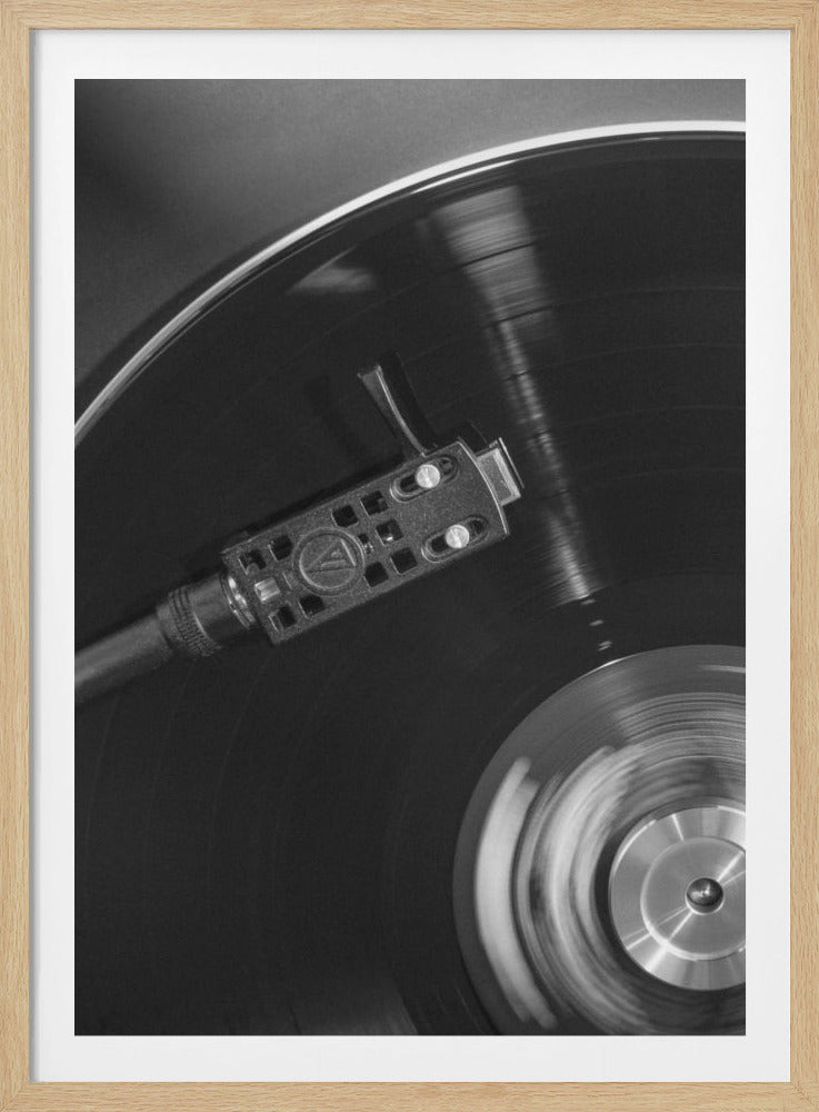 A close-up, black and white photograph of a spinning vinyl record on a turntable. The stylus on the tonearm is positioned on the record, capturing the motion and detail of the classic music player. Wall Art