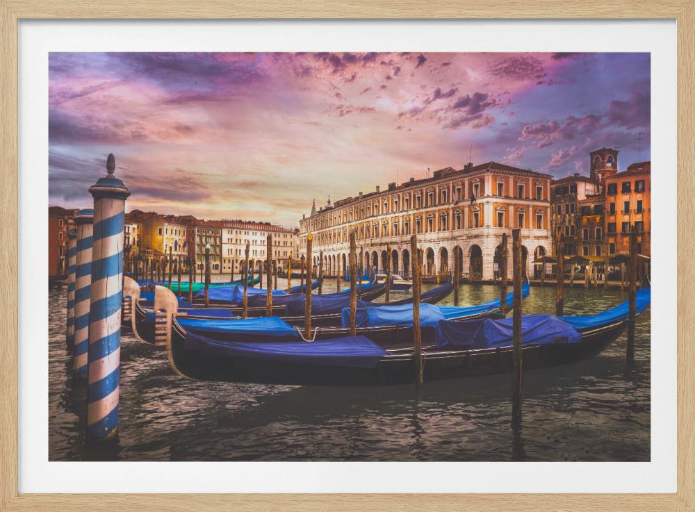 A scenic view of a Venetian canal at sunset, with several gondolas covered in bright blue tarps moored along the waterway. In the background, historic Italian buildings are illuminated by the warm light under a dramatic purple and pink sky. Artwork