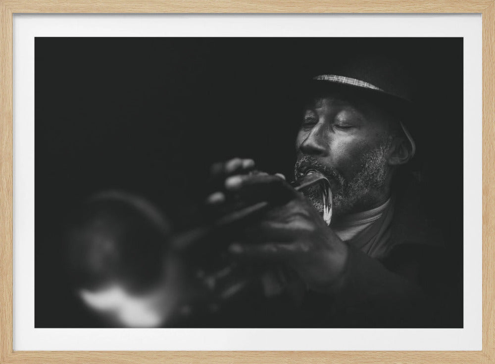 A dramatic black and white close-up photograph of an older Black man with a beard and a hat, playing a trumpet with his eyes closed in concentration against a dark background. The image is presented in a silver frame. Decor