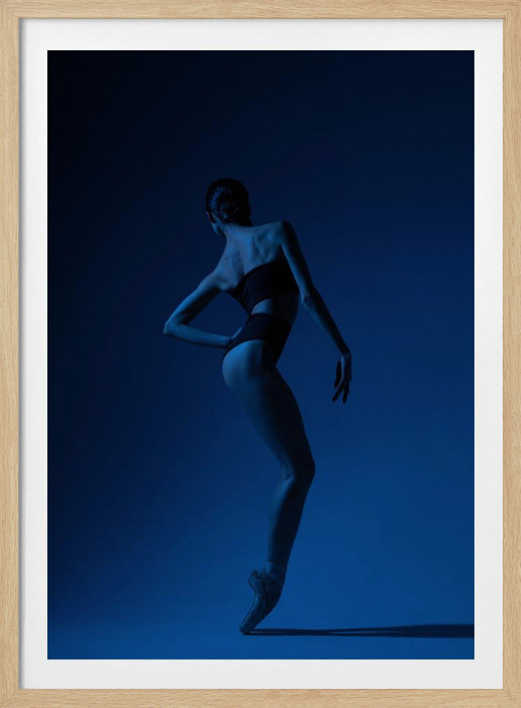 A ballerina seen from behind, bathed in dramatic blue light against a solid blue background. She is posed en pointe, with one hand on her hip and the other gracefully extended, highlighting the muscular lines of her back and legs. Poster