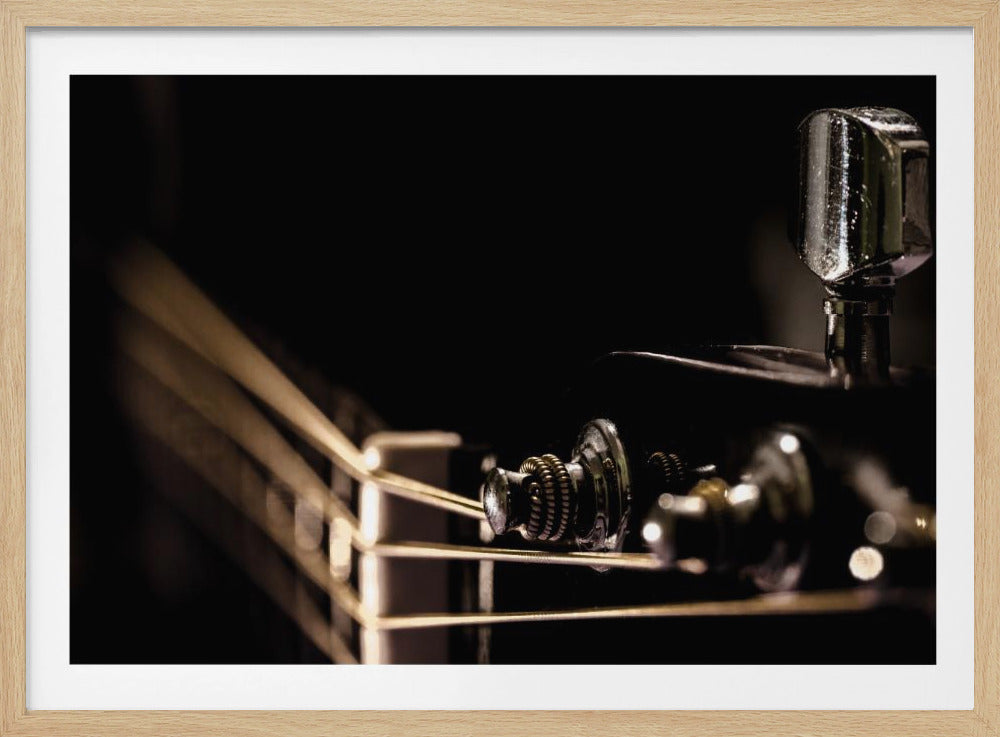 A dramatic close-up photograph of a guitar headstock in a silver frame. The focus is on the shiny chrome tuning pegs and the golden strings stretching across the nut, all set against a dark, moody background. Artwork