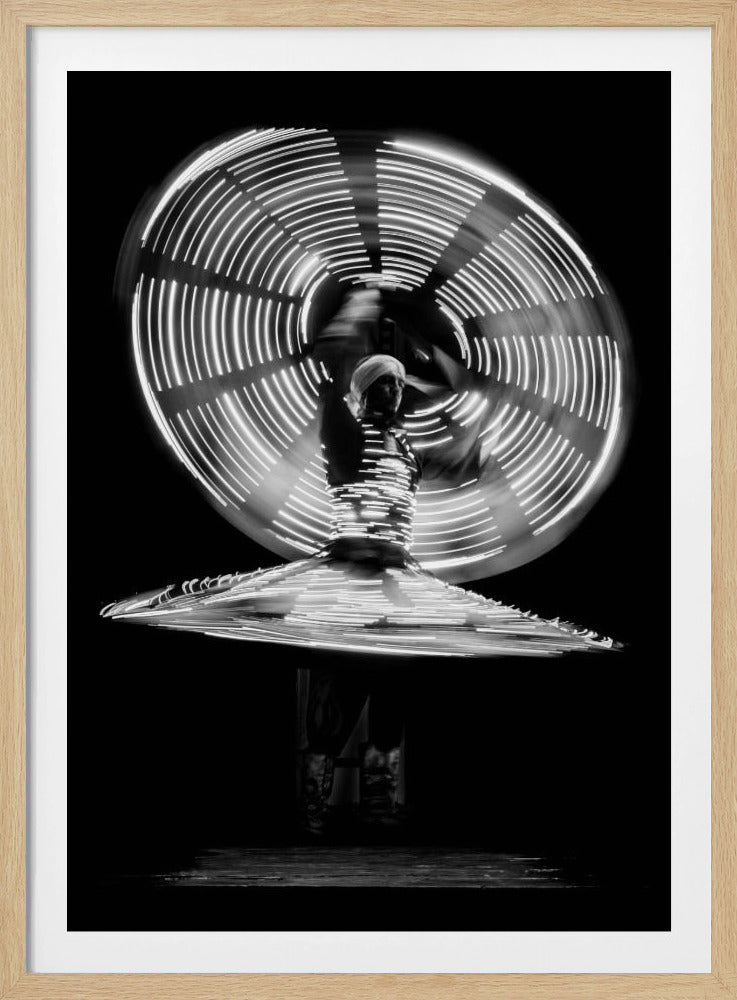 A black and white long-exposure photograph of a Tanoura dancer spinning in the dark. The dancer's costume is adorned with lights, creating mesmerizing circular light trails that form a flat disc at the waist and a large, vertical wheel of light in the background. Print