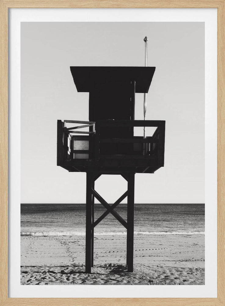 A high-contrast, black and white photograph of a silhouetted lifeguard tower standing on a sandy beach. The tower is centrally framed against a bright, empty sky, with the ocean and horizon visible in the background. Wall Art