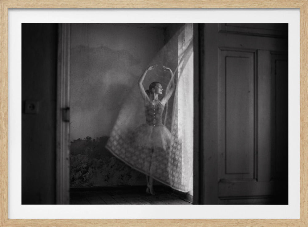 A framed, black and white photograph captures a ballerina in a graceful pose within a rustic room. She stands in a shaft of sunlight from a window, her arms raised elegantly above her head, and her tutu appears to be in motion, creating a soft, ethereal blur. Decor