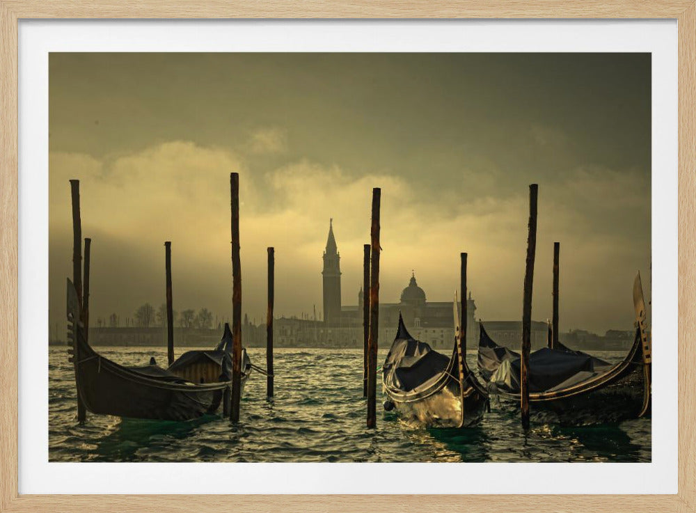 A moody, atmospheric photograph of gondolas moored in a Venetian canal during a hazy sunrise or sunset, with the iconic silhouettes of San Giorgio Maggiore and its campanile visible in the golden-lit background. Wall Art