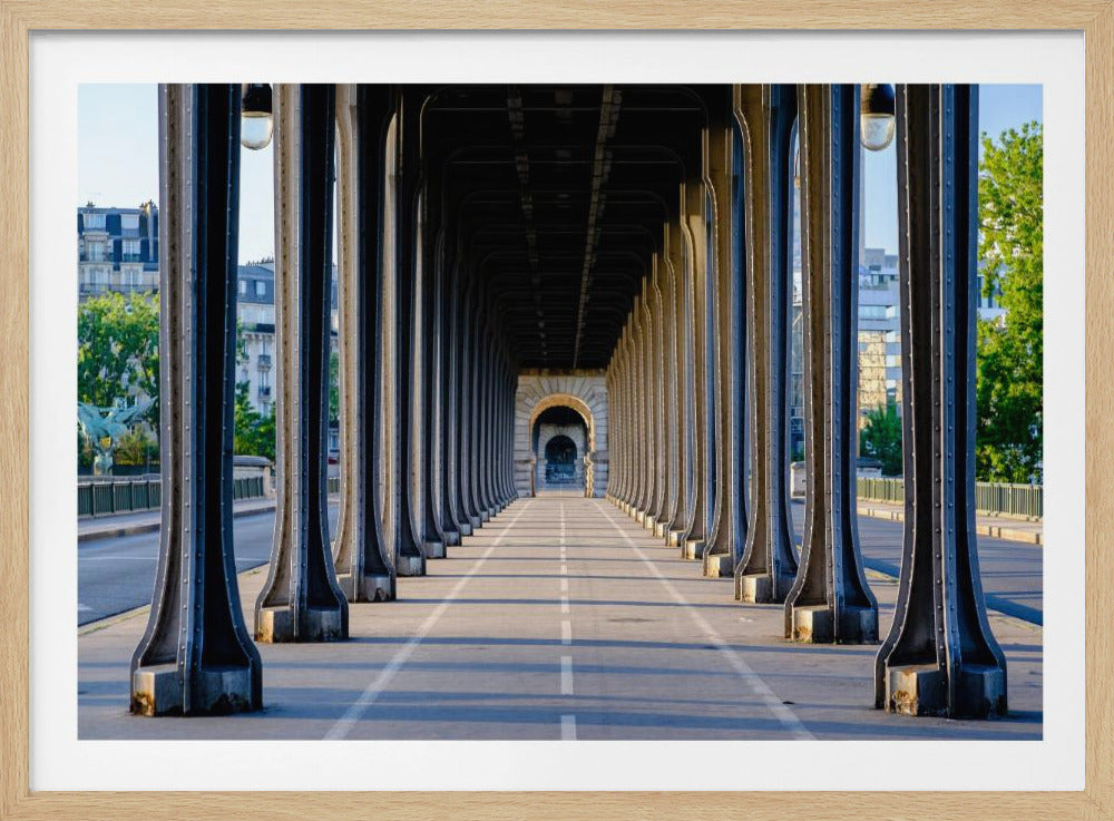 A symmetrical, long-perspective photograph from beneath a steel viaduct, showing repeating riveted columns that create a tunnel effect leading to a distant stone archway, all enclosed in a silver frame. Wall Art
