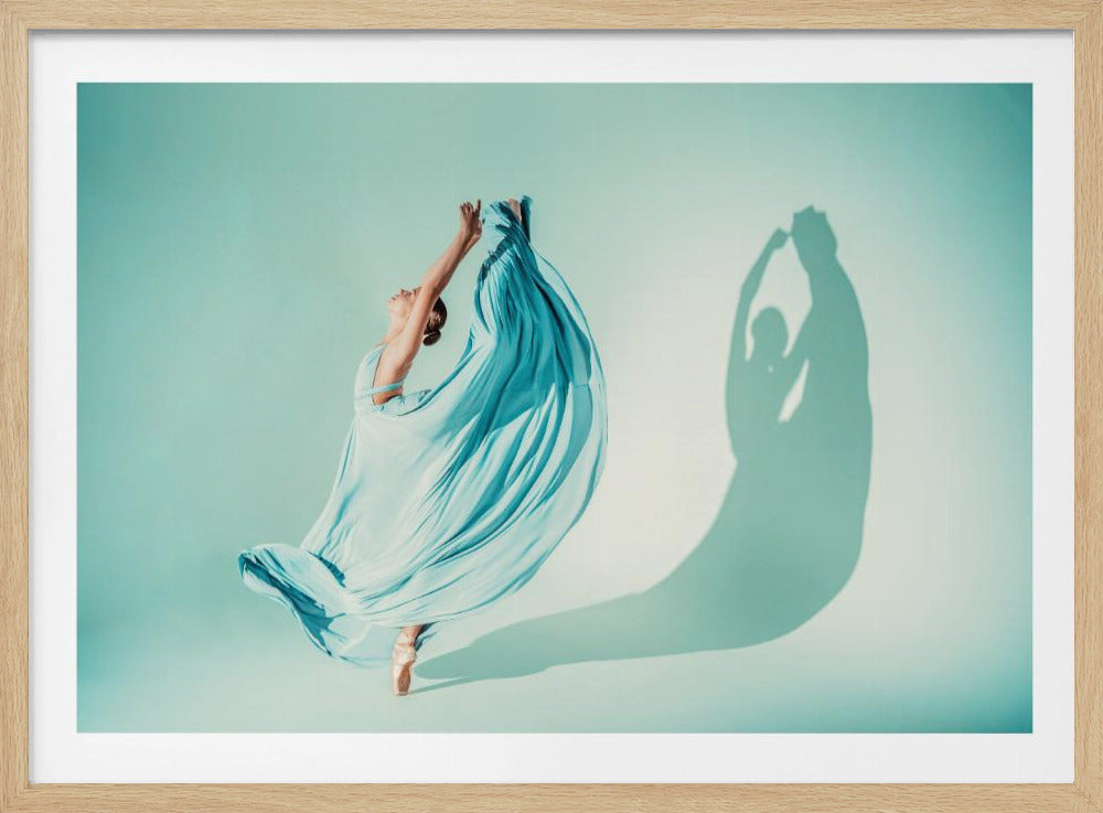 A framed photograph of a graceful ballerina on pointe, her long, light blue dress billowing out as she raises her arms, casting a dramatic shadow against a solid teal background. Decor