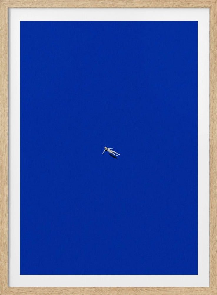 A minimalist and surreal artwork featuring a tiny, pale human figure floating peacefully in the center of an immense, solid, and vibrant blue void, all enclosed within a thin black frame. Wall Art
