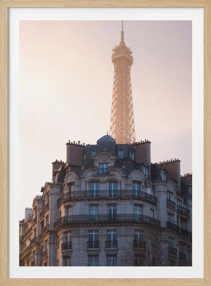 A classic Parisian apartment building with ornate balconies stands in the foreground, while the iconic Eiffel Tower rises behind it into a hazy, warm-toned sky. Poster