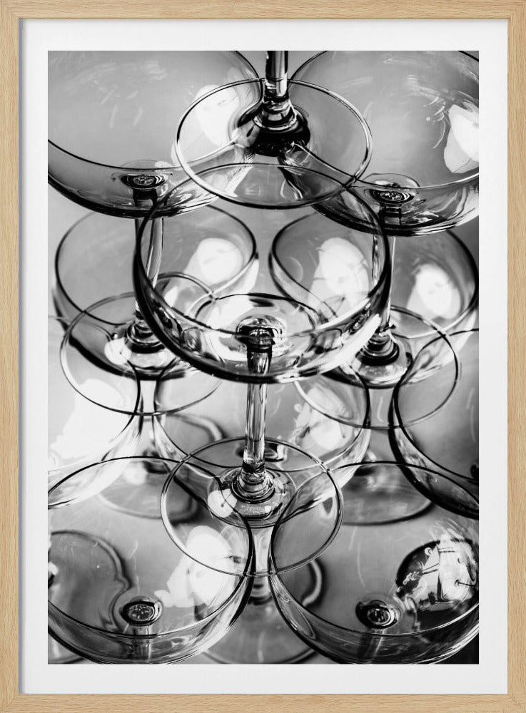 A black and white, overhead photograph of a tightly packed stack of empty champagne coupe glasses. The overlapping rims, stems, and bowls create a complex abstract pattern of circles and reflections, all enclosed within a simple black frame. Poster