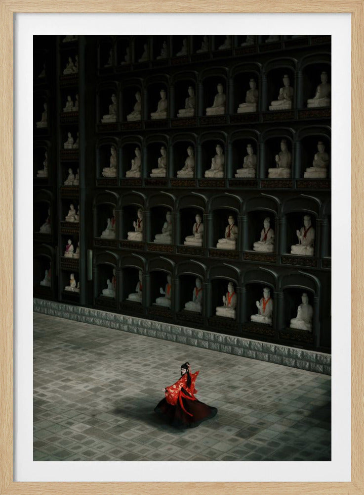 A high-angle view of a vast, dark temple hall where a lone woman in a flowing red and black traditional dress stands on a grey stone floor, dwarfed by a towering wall filled with hundreds of small, white statues in individual dark niches. Artwork