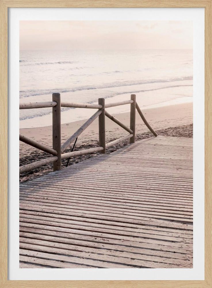 A wooden boardwalk with a rustic log fence leads down to a sandy beach with gentle waves lapping at the shore under a soft, hazy sunrise or sunset. Decor
