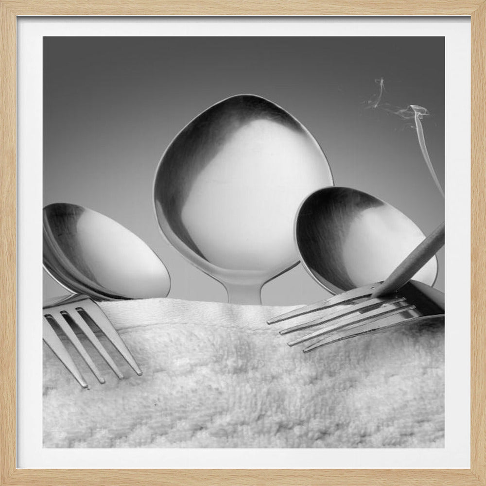 A conceptual black and white photograph in a light wood frame, featuring three spoons standing upright on a white towel, while a fork in the foreground holds a lit, smoking cigarette between its tines. Wall Art