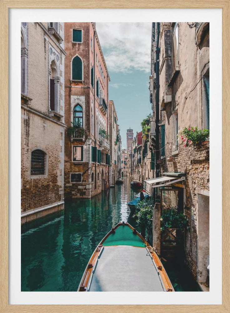 A first-person view from the bow of a boat gliding through a narrow canal in Venice, flanked by historic, weathered buildings in shades of tan and terracotta under a partly cloudy blue sky. Artwork