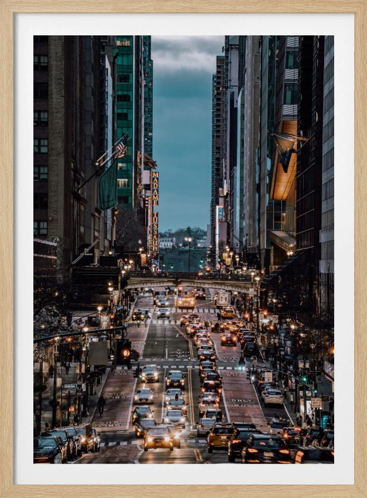A high-angle, vertical photograph looking down a bustling New York City street at dusk, framed by towering skyscrapers. The street below is packed with cars, their headlights creating a warm golden glow, contrasting with the cool, dark blue tones of the twilight sky and buildings. Poster