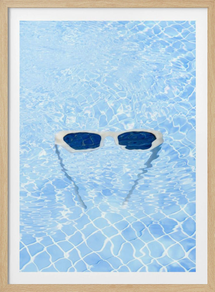 A pair of white-framed sunglasses with dark lenses floats on the surface of a bright blue swimming pool. The rippling water distorts the view of the tiled pool floor, and the sunglasses cast a faint shadow underneath. Print
