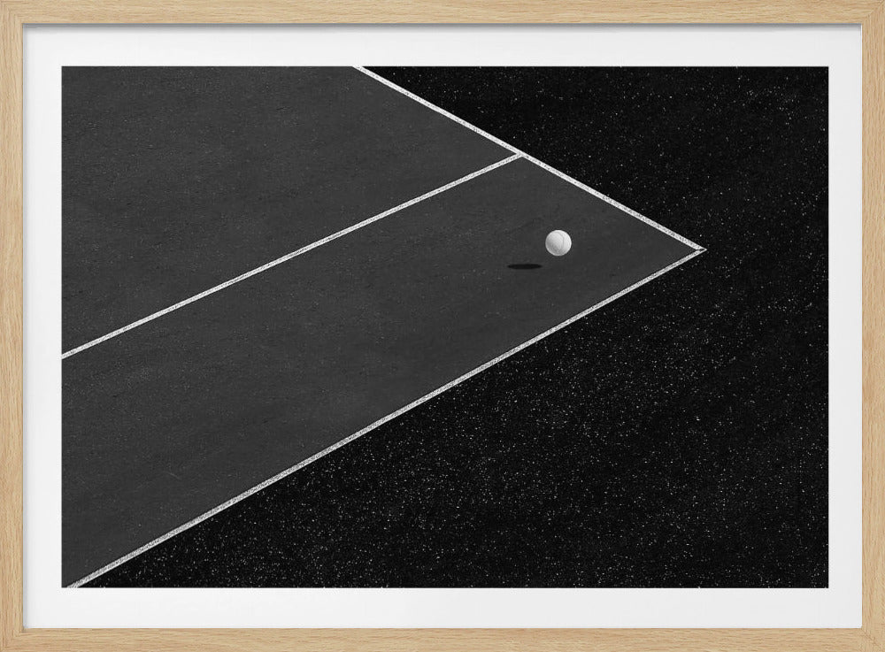 A minimalist black and white overhead photograph of a white ball resting in the corner of a dark tennis or paddle court. The composition focuses on the strong geometric angles created by the white boundary lines against the dark, textured asphalt, all within a silver frame. Artwork