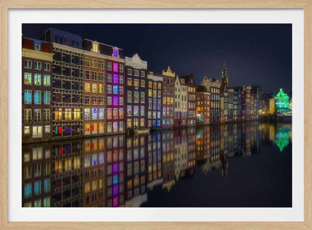 A vibrant nighttime photograph of colorful canal houses in Amsterdam, with their glowing lights beautifully reflected in the still water of the canal below, all framed in silver. Print
