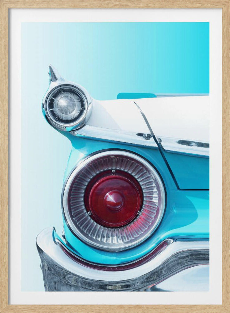 A close-up, framed photograph of the tail fin of a vintage turquoise and white car. The focus is on the large, round, red taillight and the smaller chrome-encased light on the fin, set against a solid light blue background. Poster
