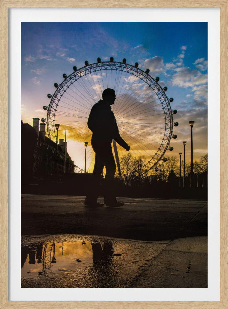 A low-angle shot of a person's silhouette walking past the London Eye at sunset, with the vibrant orange and blue sky reflected in a puddle in the foreground. Decor