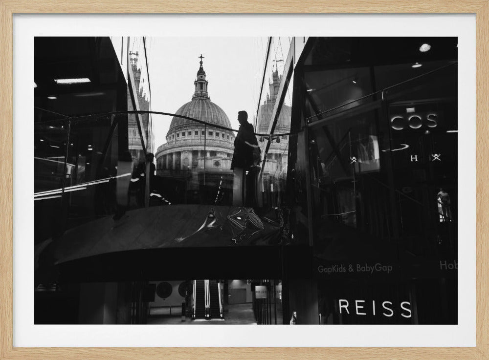 A framed, black and white photograph capturing the reflection of St. Paul's Cathedral in the glass of a modern shopping center. A person's silhouette stands on an interior balcony, juxtaposed against the historic dome, while the mall's interior and store signs are visible in the foreground. Print