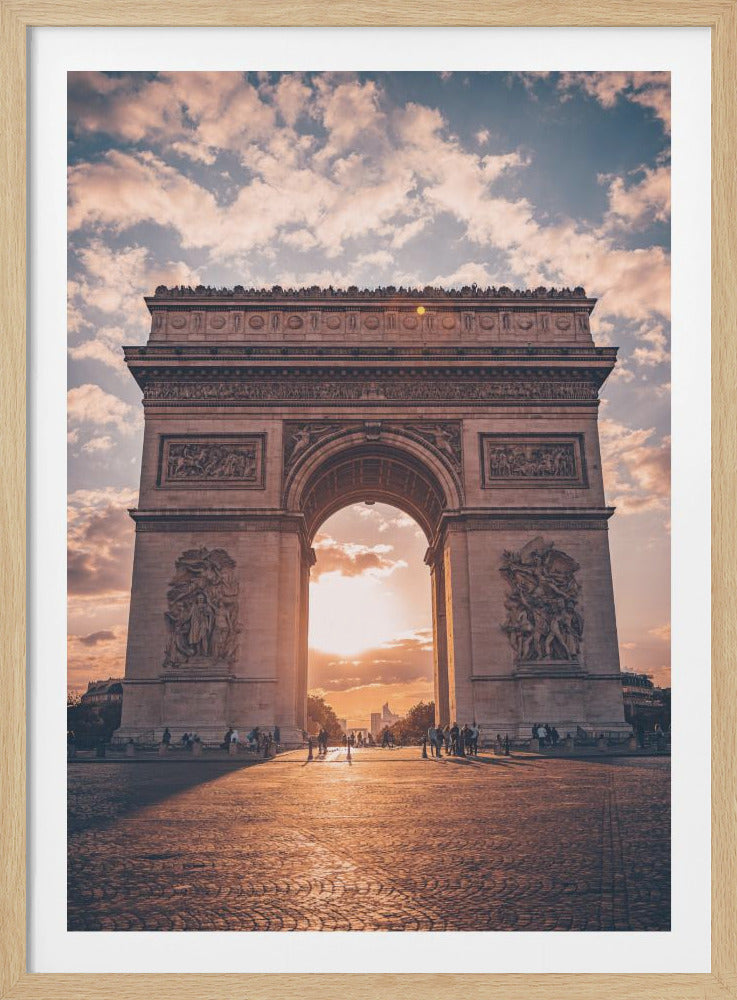A low-angle, centered photograph of the Arc de Triomphe in Paris at sunset. The golden sun sets directly behind the arch, casting long shadows and a warm glow on the cobblestone plaza. The sky above is filled with soft, pink-tinged clouds against a blue backdrop. Poster