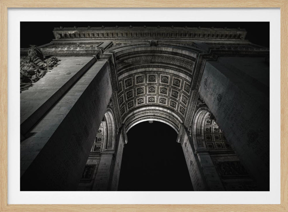 A dramatic, low-angle, black and white photograph looking up through the Arc de Triomphe at night. The intricate details of the coffered arch ceiling are illuminated against the dark sky, emphasizing the monument's grandeur. The image is presented within a silver frame. Print