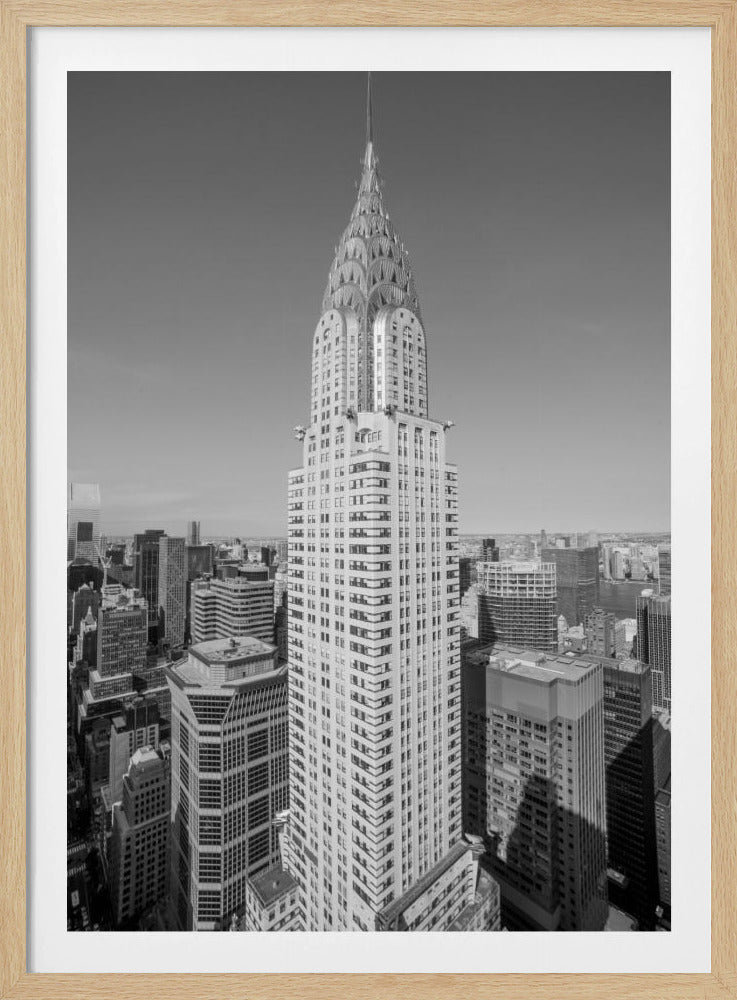A high-angle, black and white photograph of the iconic Chrysler Building, its Art Deco spire prominently featured against the New York City skyline under a clear sky. Artwork