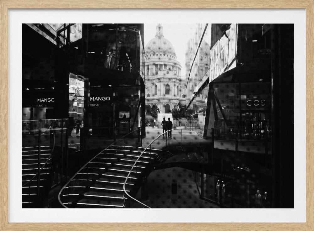 A framed, black and white photograph capturing a layered urban scene. The view, seen through a window with reflections of a curved, lit staircase, shows two people walking towards a large domed cathedral framed by modern glass buildings. Wall Art