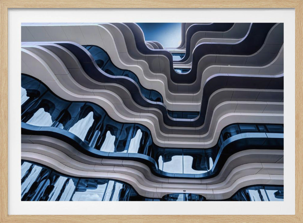 A low-angle view of a modern building with a striking, wavy facade. Alternating bands of light and dark grey create a fluid, ribbon-like pattern, with curved glass windows reflecting the deep blue sky. Artwork