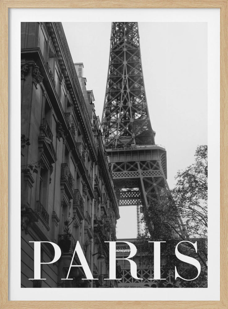 A black and white photograph of Paris, featuring a low-angle shot of the Eiffel Tower rising behind a classic Parisian building. The word 'PARIS' is written in large, white serif letters across the bottom of the image. Print