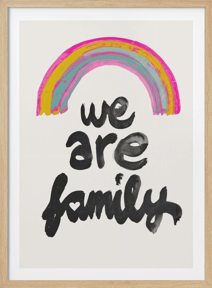 A framed art print with a hand-painted rainbow in pink, yellow, and blue at the top. Below the rainbow, the words 'we are family' are written in a black, calligraphic brush script on a white background. The 'i' in family is dotted with a small heart. Wall Art