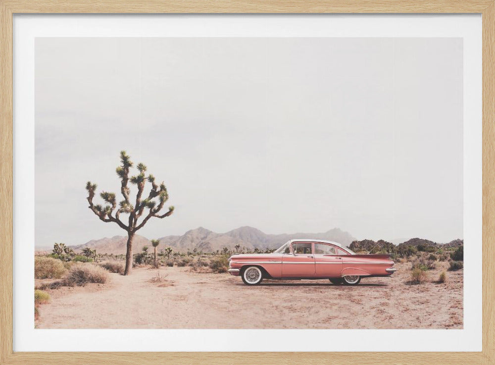 A framed photograph of a vintage pink and white sedan parked in a desert landscape. A large Joshua tree stands to the left, with distant mountains visible under a hazy sky. The scene has a warm, faded aesthetic. Print