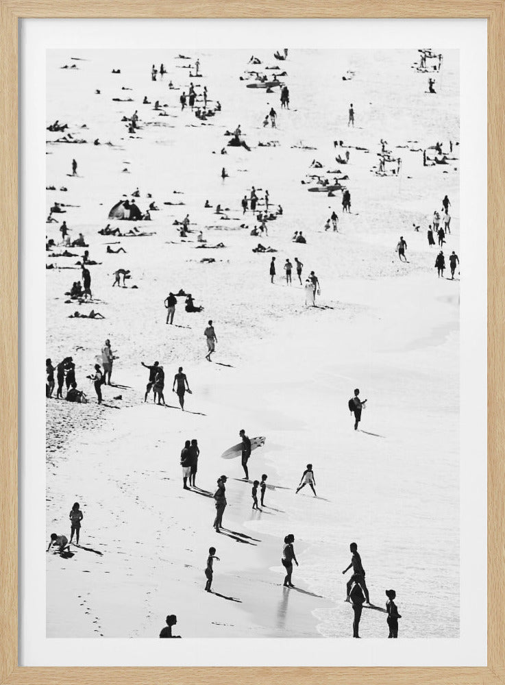 A high-contrast, black and white aerial photograph of a busy beach scene. Numerous people are depicted as dark silhouettes against the bright white sand and water, enjoying a sunny day by swimming, sunbathing, and walking along the shoreline. Long shadows stretch across the sand, indicating strong sunlight. The entire image is enclosed in a simple black frame. Print