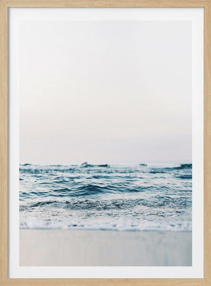 A minimalist, eye-level photograph of gentle blue ocean waves under a bright, overcast sky, enclosed in a simple black frame. The focus is on the texture of the water in the foreground. Artwork