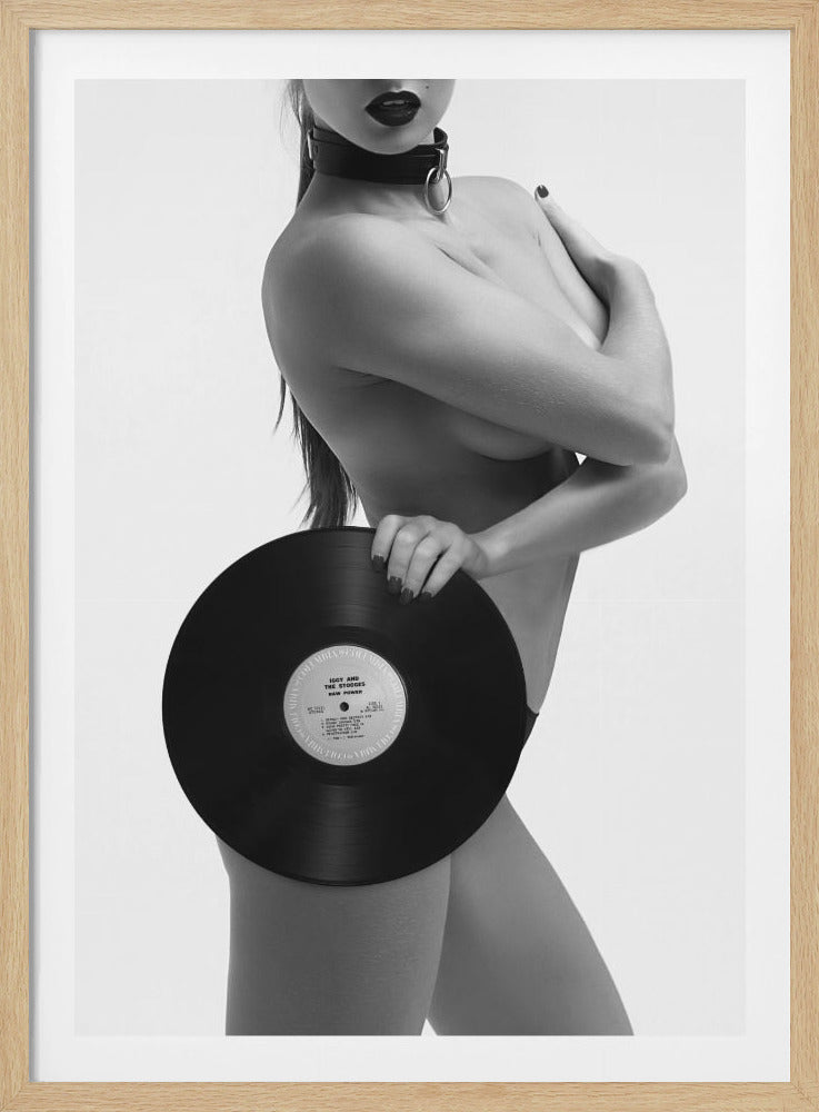 A black and white photograph of a topless woman wearing a dark choker and lipstick, covering herself with her arm and a large vinyl record against a plain background. Artwork