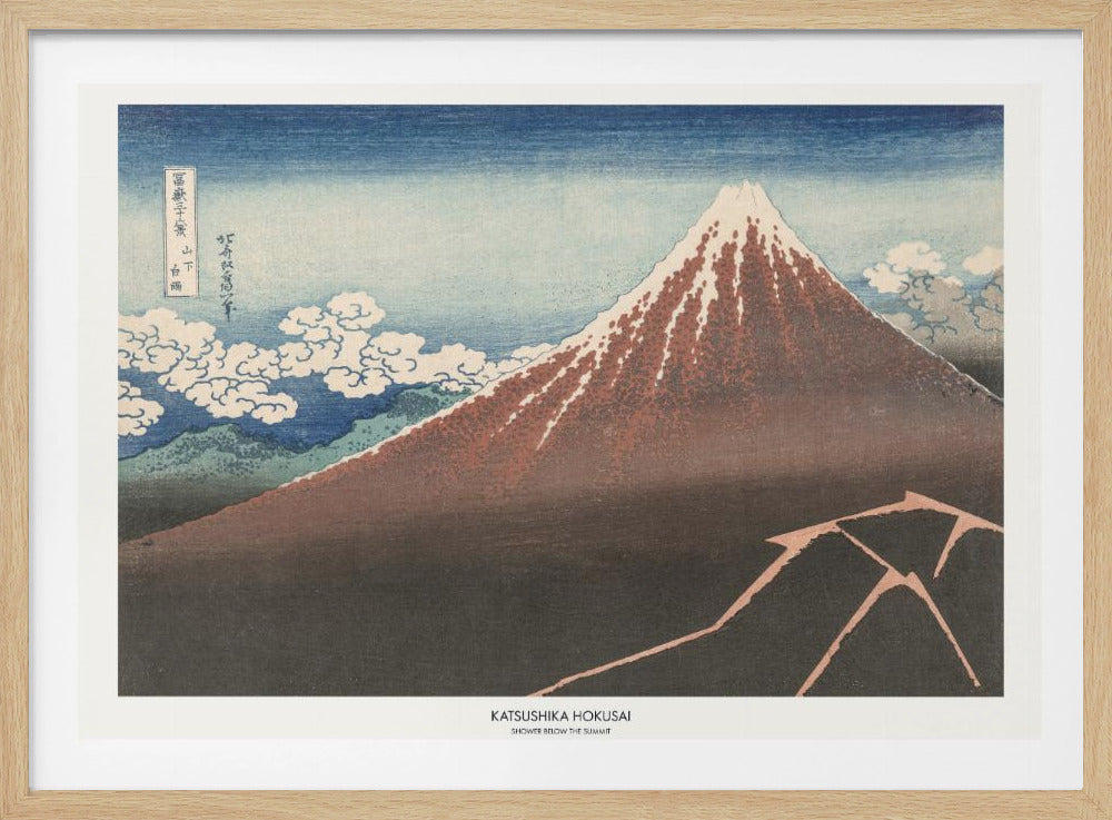 A framed Japanese woodblock print by Katsushika Hokusai titled 'Shower Below the Summit.' The print depicts a large, dark brown and reddish mountain, likely Mount Fuji, with a snow-capped peak. The sky above is a deep blue, and stylized white clouds are scattered around the mountain's slope. In the dark foreground, a jagged pink line represents a lightning strike. Artwork