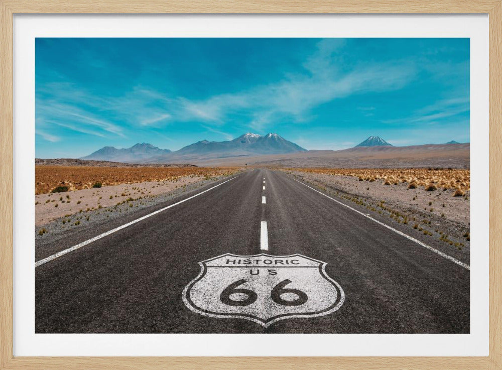 A framed photograph of the iconic Historic US Route 66 shield painted on a long, straight asphalt road that stretches through a desert landscape toward distant snow-capped mountains under a vibrant blue sky. Wall Art