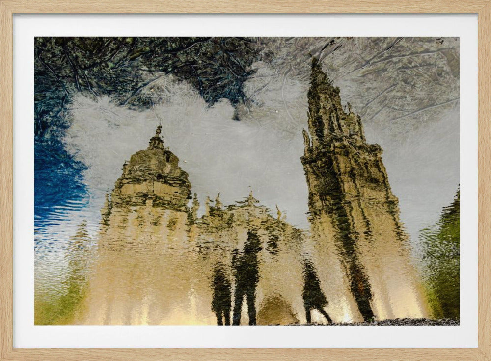 An artistic, framed photograph of a grand cathedral reflected upside-down in rippling water. The golden stone towers are distorted by the water's surface, and the dark silhouettes of people are visible in the foreground reflection. The overall effect is impressionistic and painterly. Print