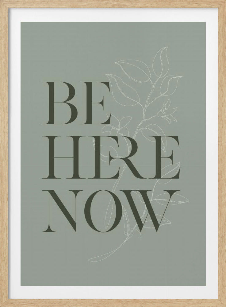 A minimalist poster in a black frame with a sage green background. The words 'BE HERE NOW' are printed in a large, dark green serif font, stacked vertically. Behind the text is a delicate white line drawing of a botanical plant stem with leaves and flowers. Decor