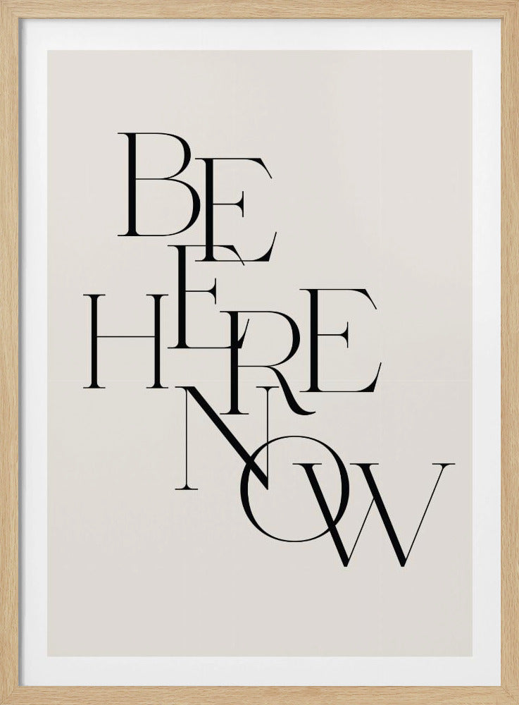 A minimalist typographic art print in a black frame. The words 'BE HERE NOW' are printed in a stylish black serif font, with the letters overlapping and stacked vertically against an off-white background. Print