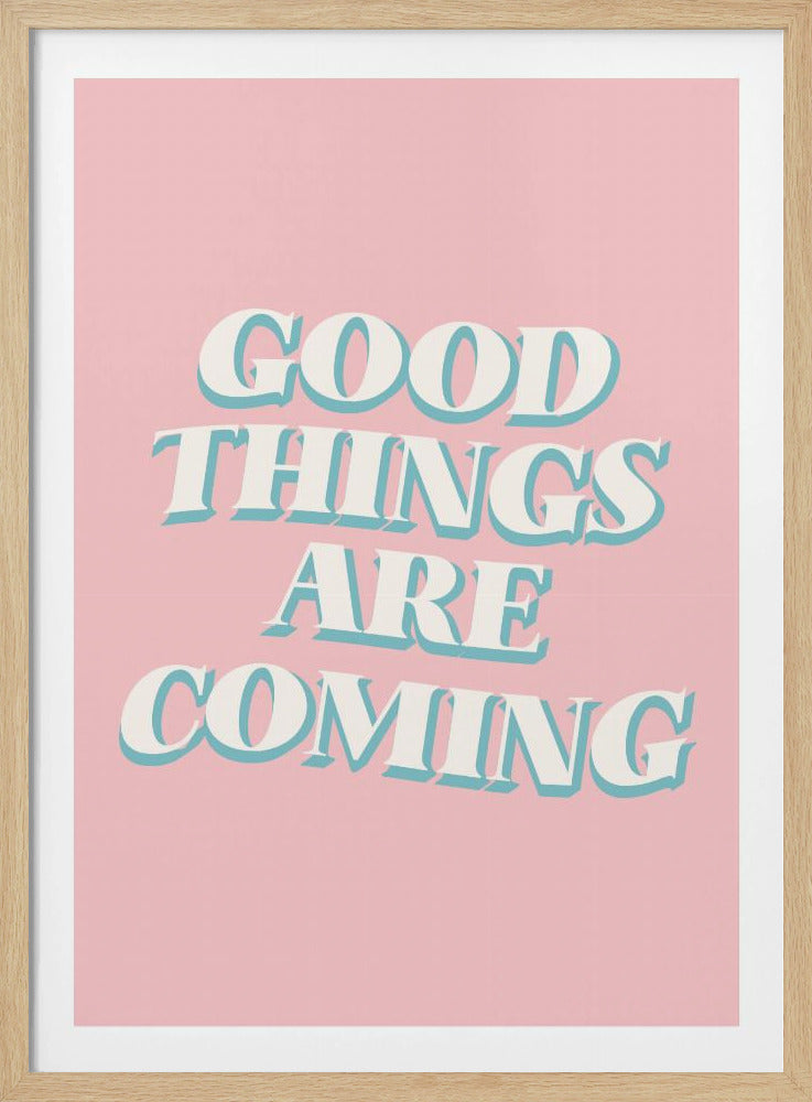 A framed poster with a light pink background featuring the motivational phrase 'GOOD THINGS ARE COMING'. The text is in a white, retro-style serif font with a light blue drop shadow, giving it a three-dimensional effect. Poster